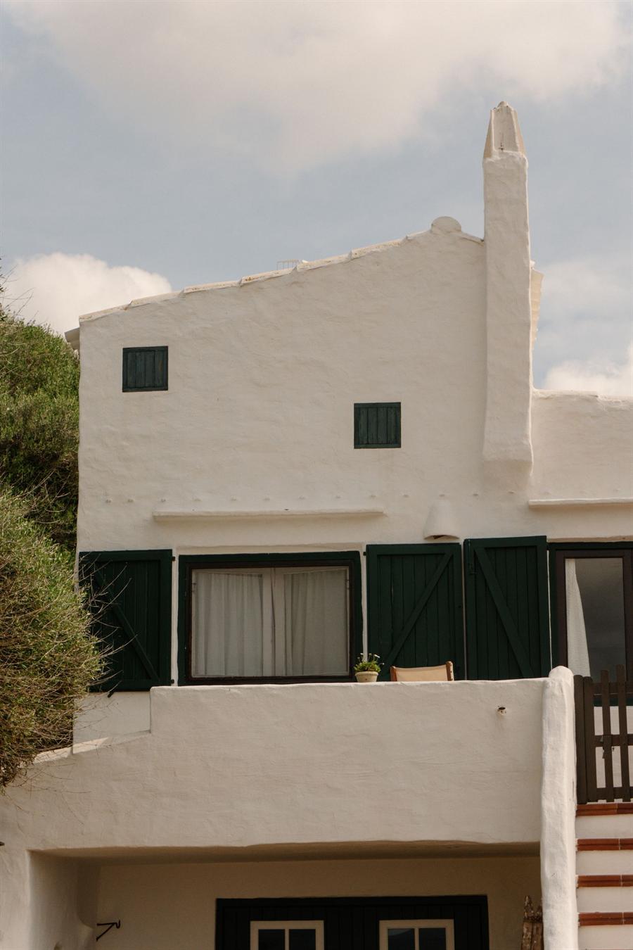 Façade de maison enduite en blanc, avec volets de bois foncé et cheminée maçonnée